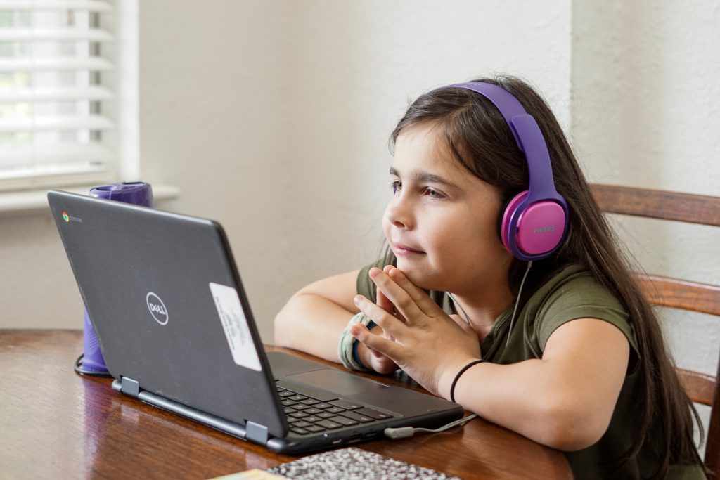 A young girl wears headphones as she completes her schoolwork on her laptop at home