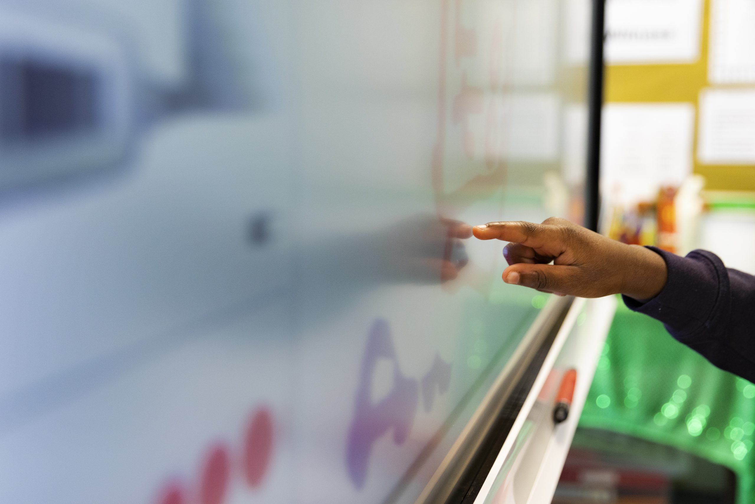 A primary school student draws on an interactive touchscreen board in a classroom