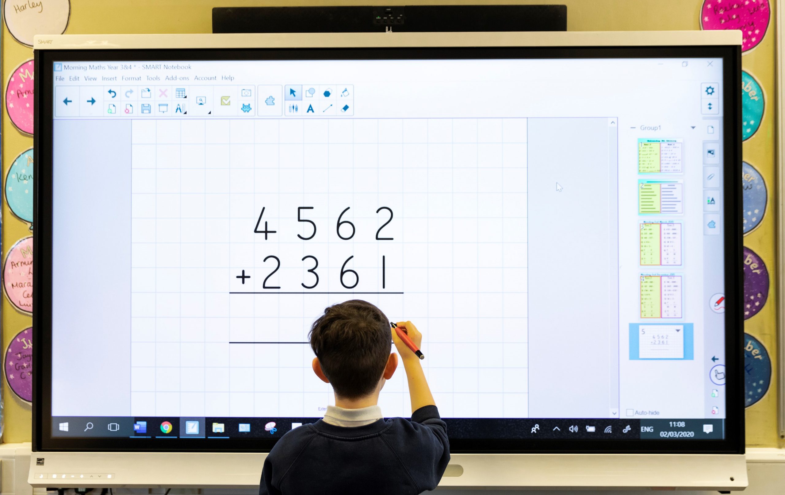 A primary pupil solves an addition problem using an interactive touchscreen board.