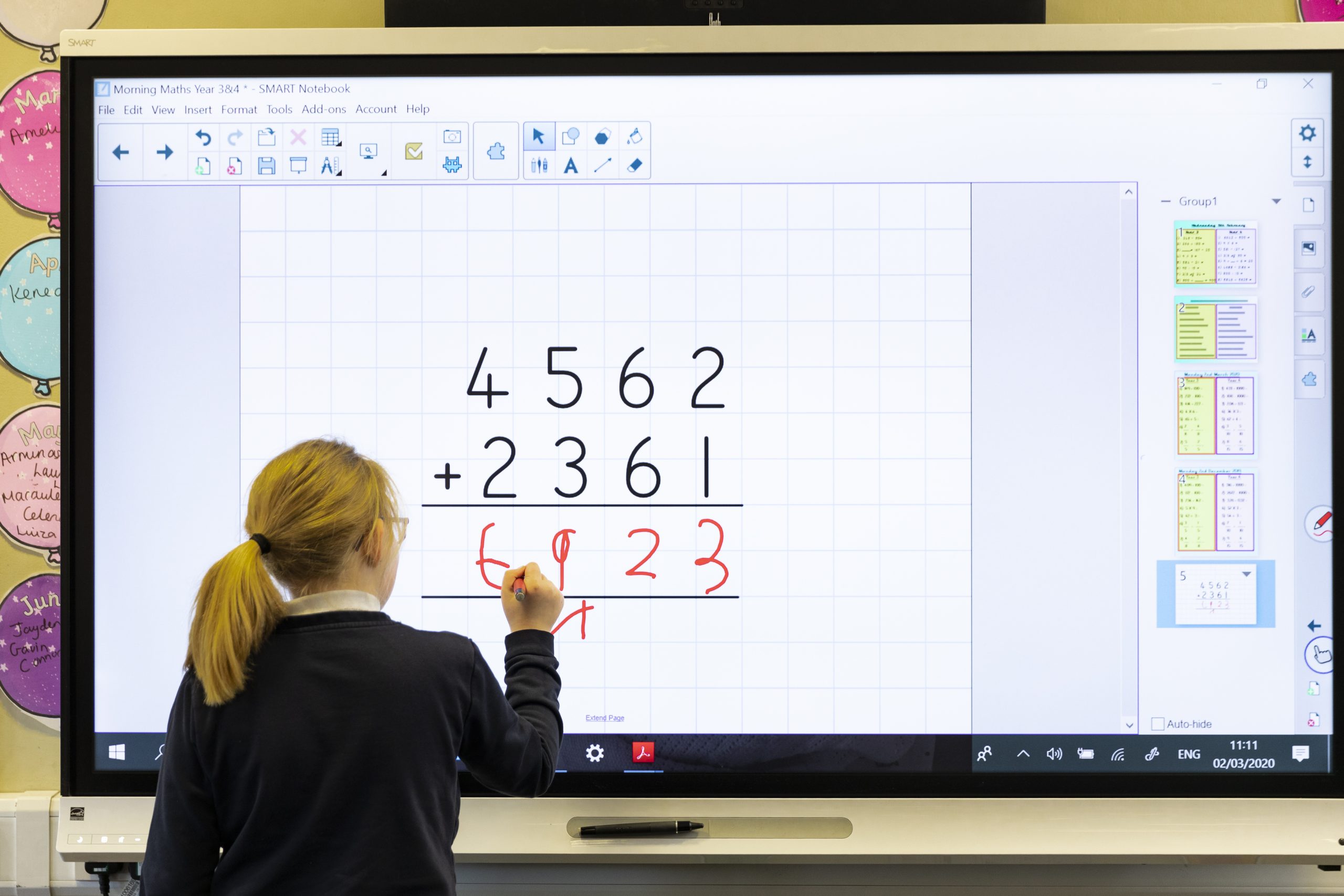 A primary school pupil solves a maths problem using an interactive touchscreen board
