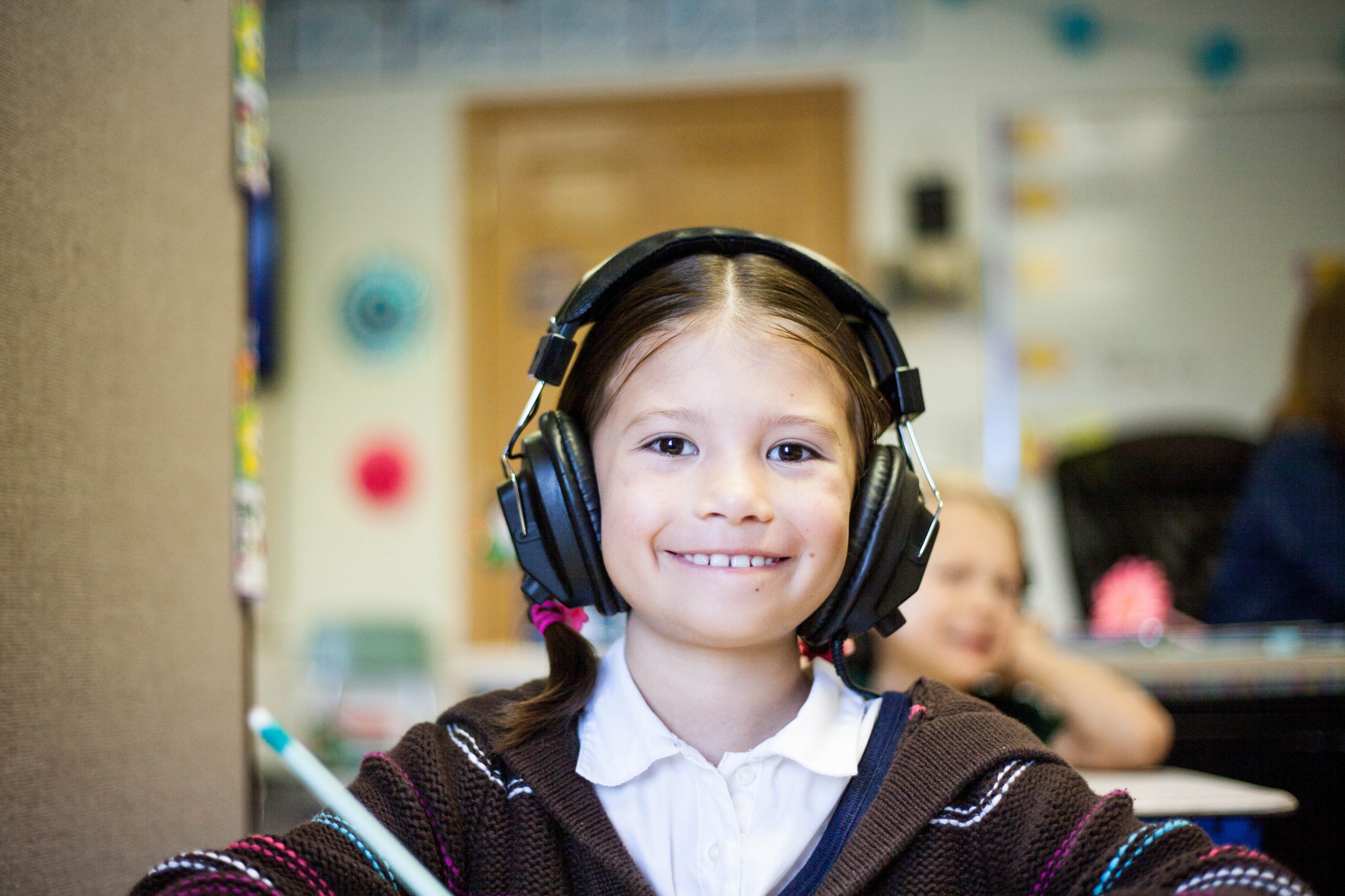 A pupil with headphones on smiles as she uses her laptop in school.