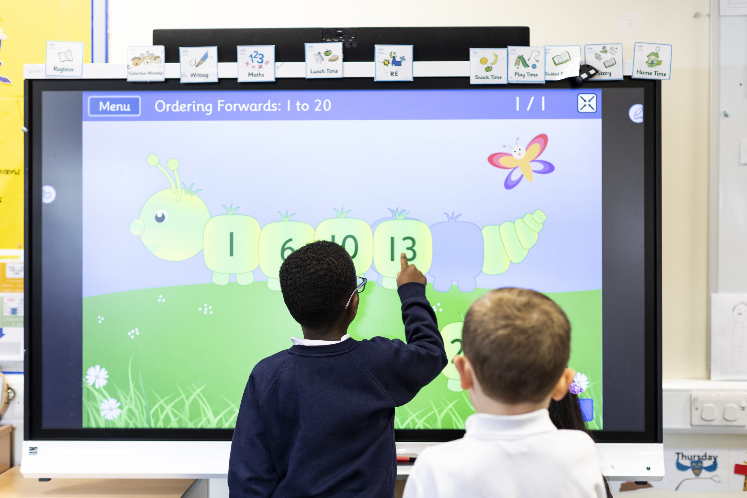 Primary pupil plays a number game on an interactive touchscreen board at the front of the classroom.