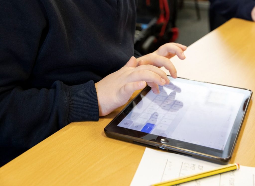 A primary school pupil uses an iPad in a classroom
